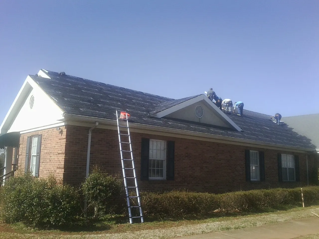 Crew tearing shingles off a brick ranch roof with a ladder set — Emergency Roof Repair work by our crew in Centerville